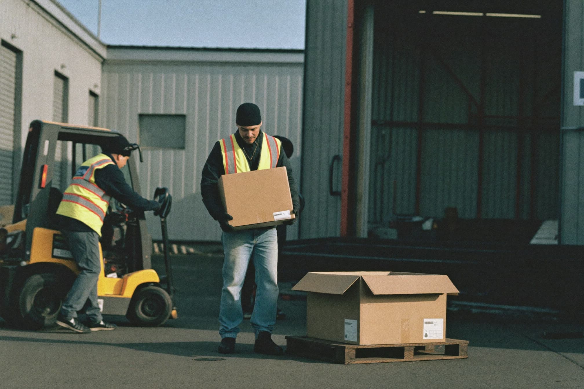 Warehouse worker in a high-visibility vest lifting a box at a loading dock